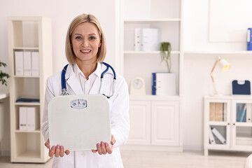 Weight loss. Smiling nutritionist with stethoscope and scales in clinic. Space for text
