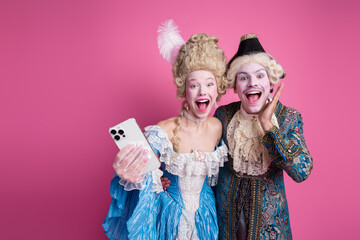 Young couple dressed in elegant baroque costumes posing playfully against a vibrant pink background