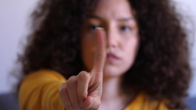 A young Hispanic woman with curly brown hair dramatically shakes her head and gestures &lsquo;no&rsquo; at the camera, clearly expressing disapproval.