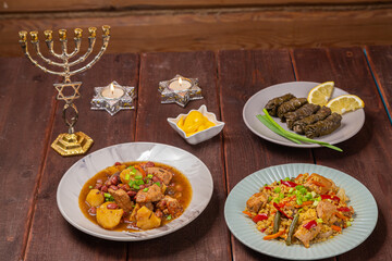 Menorah candles in candlesticks with the Star of David at the set table chelnt, bulgr dolma traditional food on Shabbat. Horizontal photo.