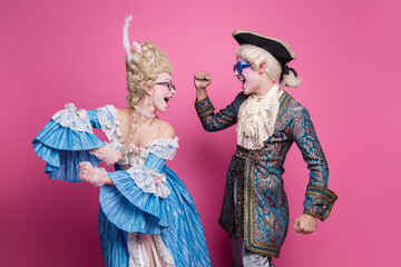 Charming couple in baroque costumes having fun against a vivid pink background, showcasing a sense...