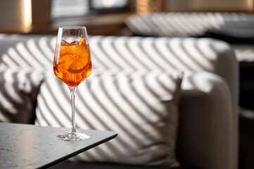 A refreshing cocktail glass filled with a vibrant orange drink, ice, and orange slice, placed on a stylish table. Soft shadows create a cozy atmosphere in a modern lounge.