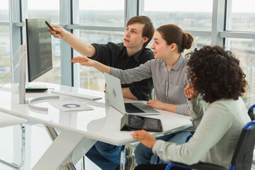 Obraz premium Teamwork brainstorm. Diverse multiracial colleagues woman in chair for people with disability working together. Group of people sitting in creative office discussing business. Young professional team