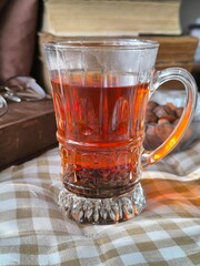 cup of black tea in a glass transparent cup against the background of books and glasses