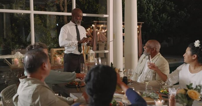 At wedding, Giving toast at elegant in backyard dinner party, man with guests