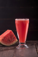 Fresh Watermelon Juice served in a tall glass with slice of watermelon on a dark background and a wooden table side view of refreshing and healthy fruit beverage