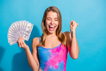 Excited woman celebrating success holding dollar bills against a vibrant blue background in a...