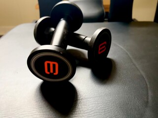  A Pilates reformer machine and a pair of dumbbells on a black leather surface, providing a combination of Pilates and strength training equipment.