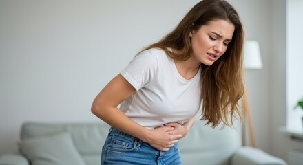 Naklejka premium Woman Experiencing Abdominal Pain - Young woman holding her stomach, showing signs of discomfort or pain. She appears to be in mild distress