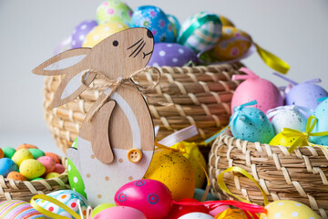 Wooden Easter bunny in white, surrounded by colorful Easter eggs on the floor in a brown wicker basket. Easter background or display.