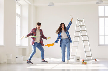 Fototapeta premium Couple joy, moving day repair, dance party in new home, happy carefree young working friends dancing having fun, energetic workers moving jumping in joy, amuse doing modern living room interior, enjoy