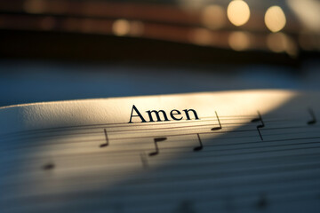 The word "Amen" appears on sheet music illuminated by soft, golden light with visible musical notes.