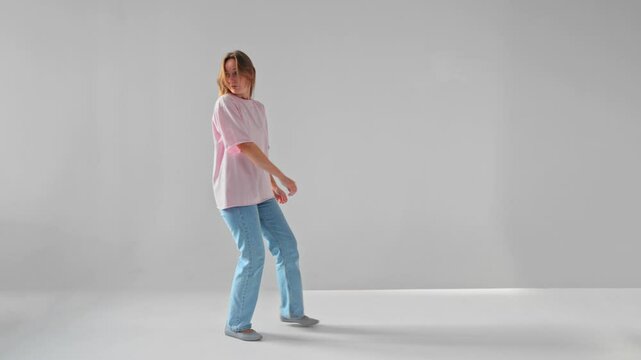 Caucasian woman is walking backwards accurately looking over her shoulder filmed against white background. Isolated slow motion footage of a young adult lady with long hair moving in reverse direction