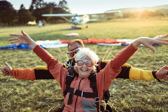 Senior woman skydiving with her instructor and landing on a field with their parachutes