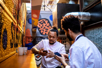 Male sushi chefs having a coffee break outside of the restaurant and using their smart phones