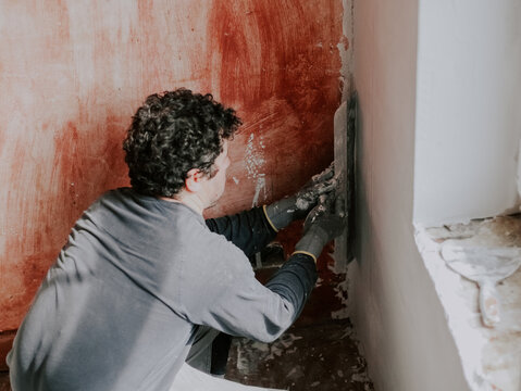 A young caucasian guy checks for evenness a fresh putty on the wall under the window