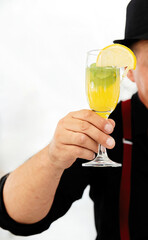 A man holds in his hand a colored cocktail with fruits in a glass glass.