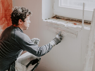 A young man is putting putty on the wall.