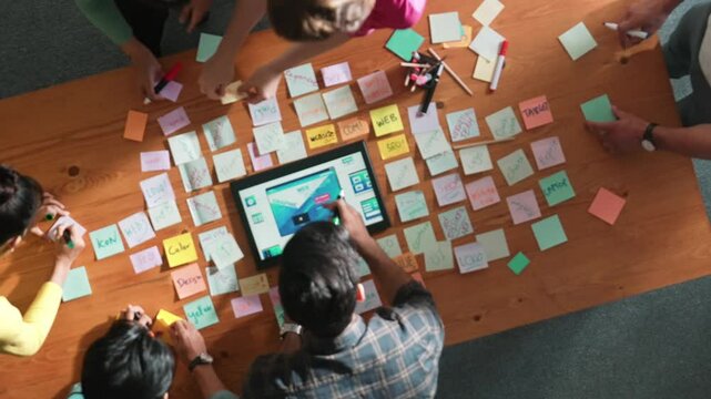 Top down view of programmer brainstorming and planning about web design while looking at tablet wireframe prototype. Aerial view of skilled developer team talking about digital application. Symposium.
