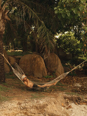 A man in a Hammock lies and smokes legal Marijuana in Thailand under the palm trees.