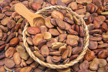A wicker bowl filled with broad beans with a wooden spoon inside