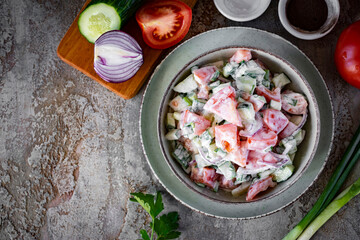 Salad of fresh vegetables in a green plate. Tomato and cucumber salad with sour cream for lunch. Close-up