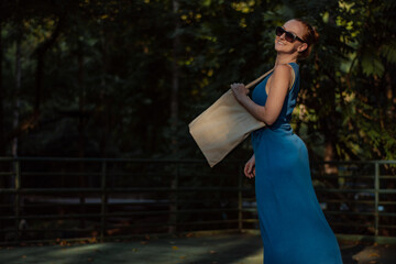 woman walking in the park in a blue dress holding a sustainable ecobag