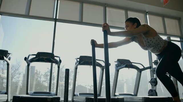 Female athlete pushes weighted sled in a gym