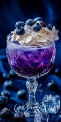 Cóctel de arándanos con crema batida y azúcar glas en una copa de cristal sobre un fondo azul oscuro.