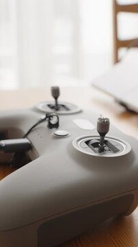 Vertical video. FPV Drone Joystick Controller with Cable Connected Sitting on Wooden Desk Next to Laptop in Natural Light, Side Angle, Setup Concept