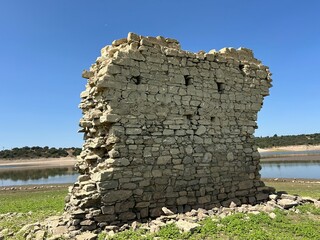 Ancient stone wall ruins near drought-affected lake under clear sky