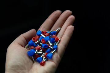 Open hand holding a pile of blue and red double ferrules (metal and plastic electrical wire...