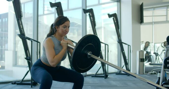 Young woman performs a glute workout with a barbell in a gym