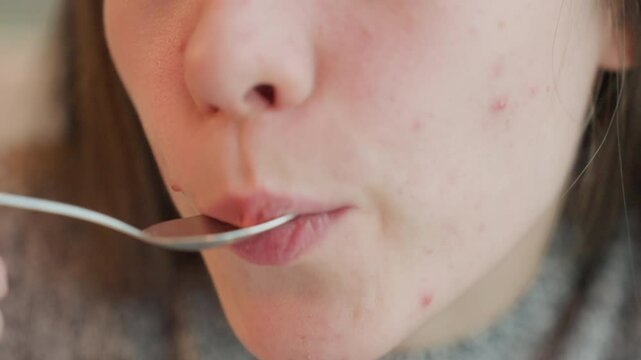 Beautiful fair lady sips coffee with spoon and licks spoon playfully in satisfaction, close up of her lips and spoon with blurred indoor setting, capturing moment of joy and indulgence