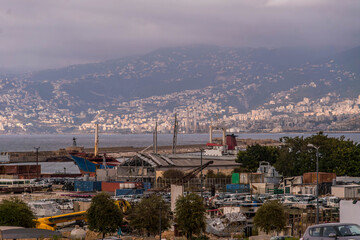 Obraz premium A panoramic view of Beirut port, Lebanon, with industrial port cranes, harbor activity, and a hilly landscape under an overcast sky. 