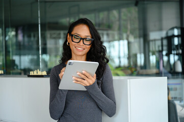 Professional Asian Businesswoman With Glasses Reading Digital Tablet In Contemporary Corporate...