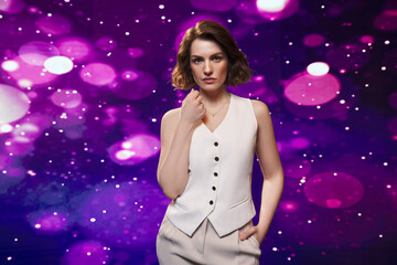 Stylish confident woman wearing a white vest and beige pants, posing against a dazzling purple...