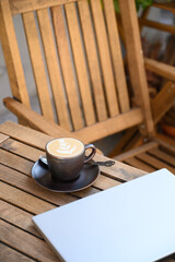 A modern workspace with a laptop and cappuccino on a wooden table in an outdoor setting. Warm natural tones and soft lighting create a productive yet relaxing atmosphere for remote work.