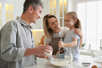 Happy parents and their daughter making dough at white marble table in kitchen