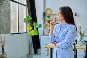 Portrait of serious middle aged woman looking out window in home