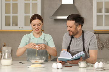 Happy couple cooking by recipe book in kitchen
