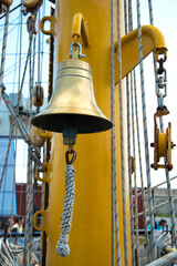 Small ship bell hanging on a rope from an old rusty anchor. Sea background. Selective focus.
