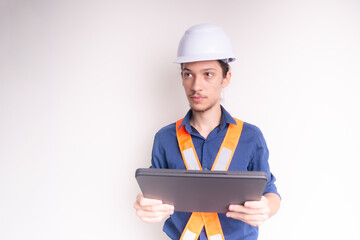 Young architect wearing white helmet and luminous vest, working with laptop. Isolated on white background.