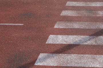 Bright white stripes of a crosswalk stand out against a reddish asphalt surface in a city street...