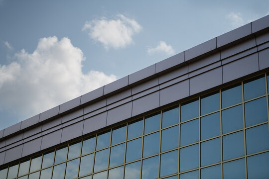 A sleek building features a reflective glass exterior that gleams under the bright sun. Soft clouds add a serene touch to the clear blue sky above the structure