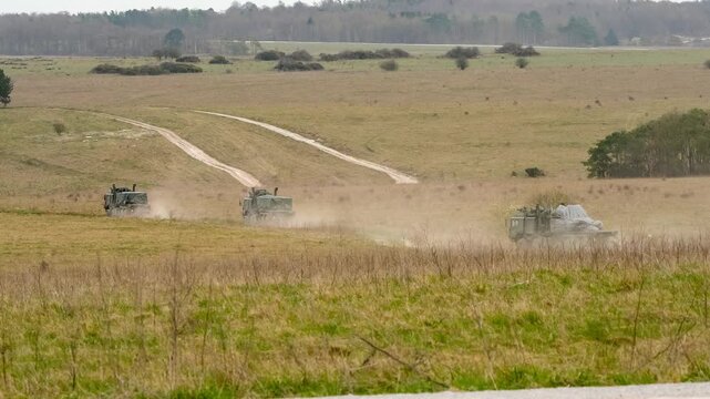 convoy of British army MAN EPLS 8x8 eight wheeled logistic trucks carrying supplies across countryside