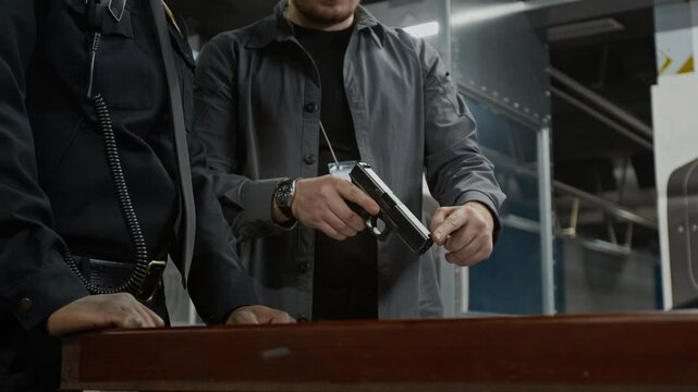 Medium shot of Caucasian male shooting coach teaching black policeman in uniform handgun handling basics, showing how to hold weapon, aim and position finger on trigger for firing
