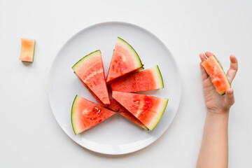 Childs hand holding watermelon slice on white plate with triangular pieces