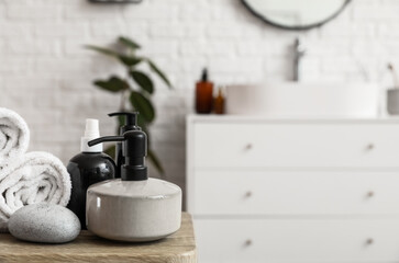 Soap dispenser, pebbles and rolled towels on table in bathroom, closeup