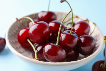Bowl with sweet cherries on blue background